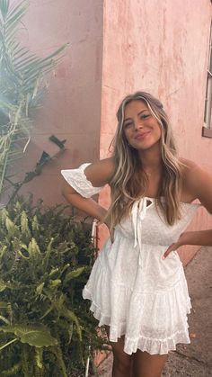 a woman standing in front of a bush with her hands on her hips and smiling at the camera