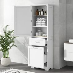 a white cabinet with towels and other items in it next to a plant on the floor