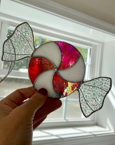 a hand holding a stained glass pinwheel in front of a window with white trim