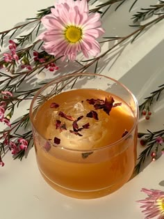 a glass filled with liquid next to pink flowers