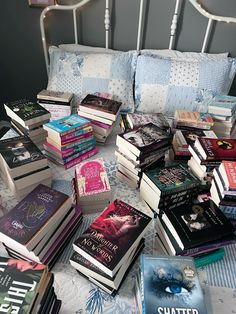 a pile of books sitting on top of a bed next to a white headboard