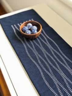 a wooden bowl filled with blueberries sitting on top of a white tablecloth next to a window