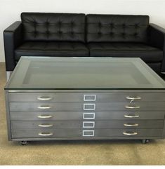 a black leather couch sitting next to a coffee table with drawers on each side and a glass top