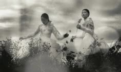 two women in white dresses are walking through tall grass