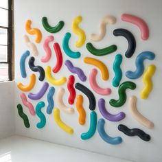 a colorful wall sculpture made out of plastic worms on a white wall with windows in the background