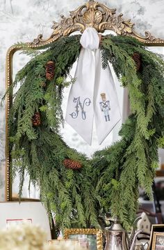 a christmas wreath with pine cones and evergreens hanging from the front of a mirror