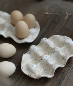 some eggs are sitting in white dishes on a wooden table with one egg laying next to the other