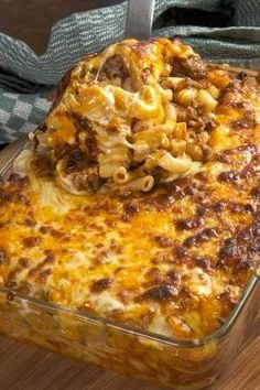 a casserole dish with meat and noodles in it on a wooden table next to a fork