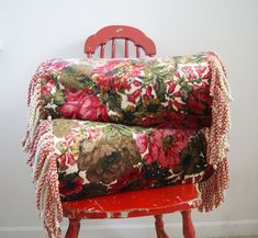 a red chair with a flowered blanket on top of it, sitting in front of a white wall