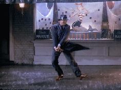 a man is dancing on the street in front of a store window with an umbrella