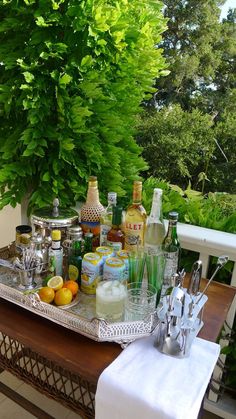 an image of a tray full of drinks and liquors on a table with trees in the background