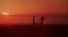 two people walking across a field with the sun setting in the backgrounnd