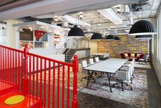 an office with red railings and white tables in the center, surrounded by black pendant lights