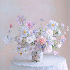 a vase filled with lots of flowers sitting on top of a white table covered in lace