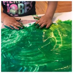 a child is painting with green paint on the paper and it looks like they are holding hands