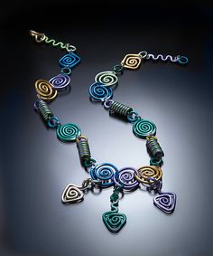 a multicolored necklace is displayed on a black surface with the word love spelled in cursive letters