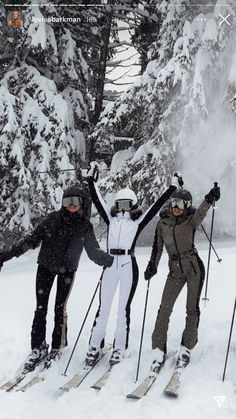 three people on skis standing in the snow with their hands up and arms raised