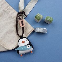 a penguin keychain and two dices on a blue background with a drawstring bag