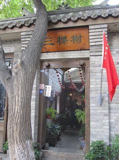 an entrance to a chinese restaurant with flags hanging from it's roof and trees in the foreground