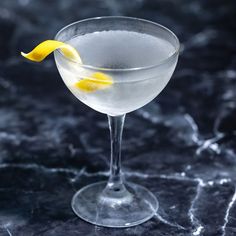 a martini glass with a lemon peel in it on a marble countertop, ready to be served