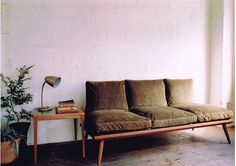 a couch sitting in front of a window next to a table with a potted plant on it