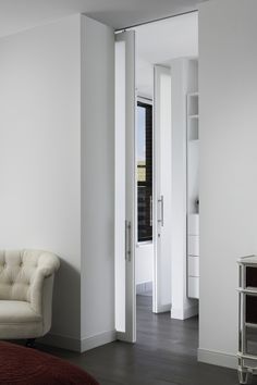 a white room with a couch and chair in it, next to an open door