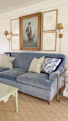 a living room with blue couches and pictures on the wall above them in gold frames