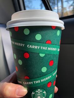 a starbucks cup with green and red polka dots is being held up by someone's hand