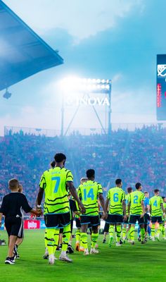 a group of soccer players walking onto the field at a game in front of an audience