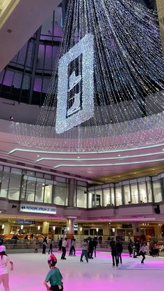 people skating on an ice rink with lights hanging from the ceiling