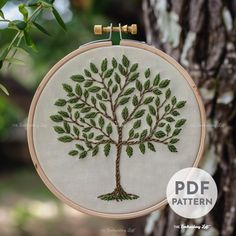 an embroidered tree with green leaves on it is hanging from a wooden hoop in front of a tree