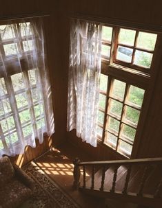 the sun shines through two windows in a room with wood floors and white sheer curtains