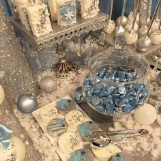 blue and white candies are in a bowl next to silver spoons on the table