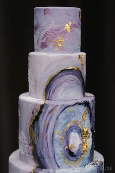 a three tiered cake with purple and gold designs on it's sides, sitting on top of a table