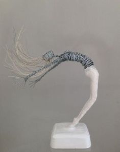 a sculpture of a woman's head on a white pedestal with long hair blowing in the wind