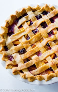 a pie with latticed crust and blueberries on top sits on a white plate