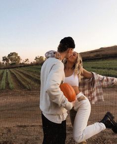 a man and woman kissing while holding pumpkins