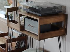 an old record player sits on top of a wooden shelf next to a chair and window