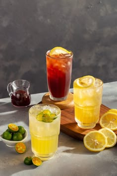 three glasses filled with lemonade and limes on top of a wooden cutting board