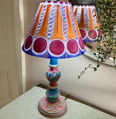 two colorful lamps sitting on top of a table next to a potted green plant