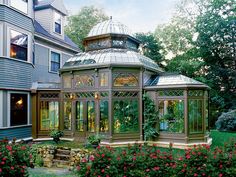 a green house with a glass roof in the middle of some bushes and flowers around it