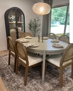 a dining room table and chairs in front of a large window with an area rug on the floor