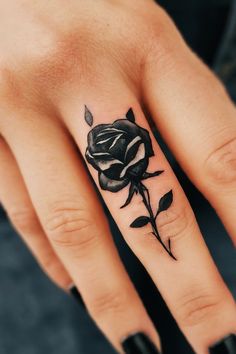 a woman's hand with a black rose tattoo on the middle finger and ring