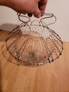 a person holding a wire basket over a wooden table with an object in the middle