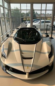 a white sports car is parked in a showroom with large windows and lots of cars behind it