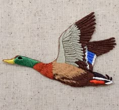 a colorful bird embroidered onto a piece of fabric on a white surface with an orange, green, and brown color scheme