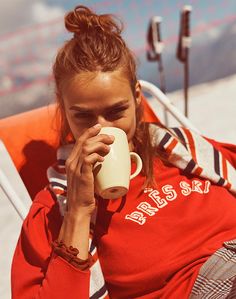 a woman sitting in a chair drinking from a cup