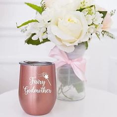 a vase filled with white flowers next to a pink and silver wine glass that says godmoter