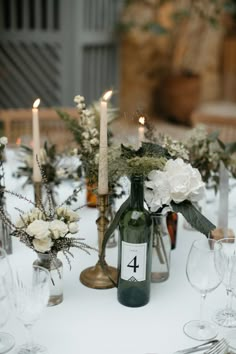 the table is set with wine bottles, candles and floral centerpieces in glass vases