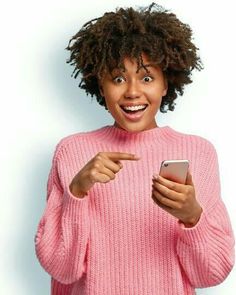 a woman in a pink sweater is holding a cell phone and pointing to the screen